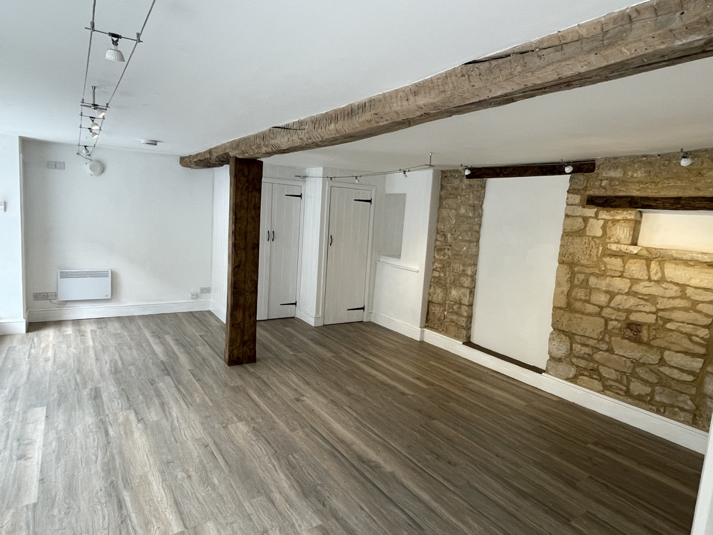 An open-plan room with a rustic and modern aesthetic. Centered on the picture is a rough stone wall which spans the width ...