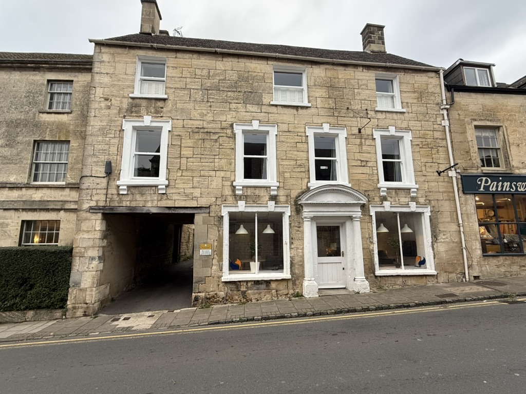 The image is a photograph of a three-story building with a tan brick exterior, white window frames and trimmings, and a da...