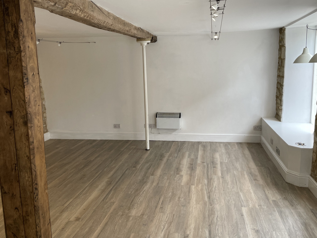 An empty room featuring a stone wall, wood floors, and a wooden beam.